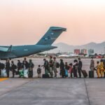 File photo (23 August 2021): Afghan evacuees, including women and children carrying luggage, wait to board a C-17 transport aircraft at Hamid Karzai International Airport in Kabul during the 2021 evacuation. Photo: Sgt. Isaiah Campbell, US Marine Corps (public domain), via Wikimedia Commons.