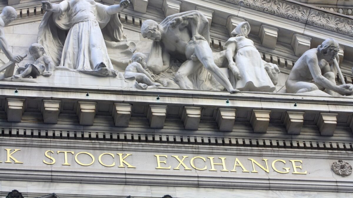 Detail of the carved stone facade of the New York Stock Exchange building in New York, with its gold-lettered STOCK EXCHANGE inscription below classical sculptures.
