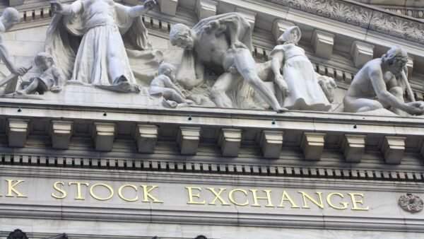 Detail of the carved stone facade of the New York Stock Exchange building in New York, with its gold-lettered STOCK EXCHANGE inscription below classical sculptures.