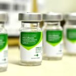 Vials of H1N1 influenza vaccine with green and white labels arranged on a table.