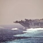 The aircraft carrier USS Abraham Lincoln and the guided-missile cruiser USS Cape St. George transit the Strait of Hormuz, with a helicopter flying nearby.