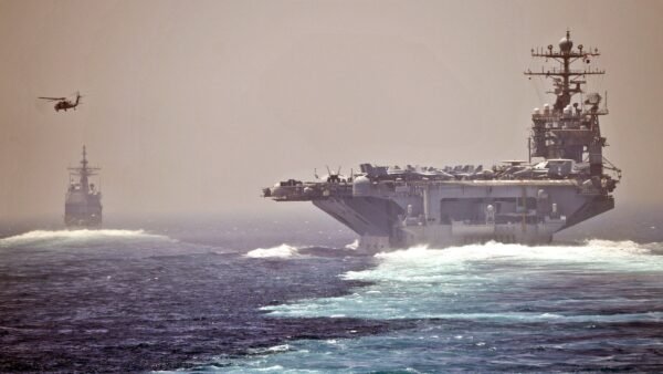 The aircraft carrier USS Abraham Lincoln and the guided-missile cruiser USS Cape St. George transit the Strait of Hormuz, with a helicopter flying nearby.