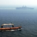 File photo: a merchant ship transits the Strait of Hormuz with the USS Kearsarge in the background.