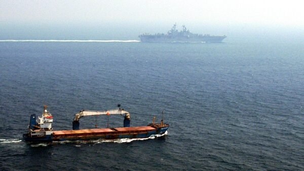 File photo: a merchant ship transits the Strait of Hormuz with the USS Kearsarge in the background.