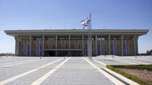 The Knesset building in Jerusalem, with Israeli flags flying in front of the parliament's stone facade.