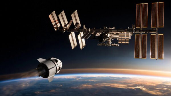 International Space Station with a departing SpaceX Crew Dragon capsule above the Earth's horizon at orbital dawn