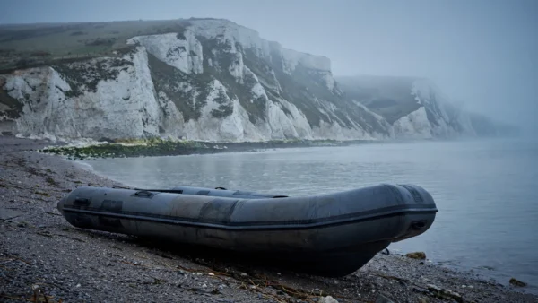 Grey rubber dinghy abandoned on a shingle beach below white chalk cliffs on the English coast