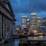 Canary Wharf financial towers glowing at dusk beside a historic London facade.