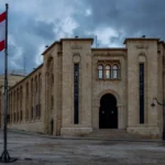 Lebanese parliament building in Beirut under a dramatic overcast sky with the Lebanese flag flying.