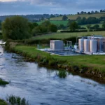 A clear British river flowing past a small water treatment plant at dusk, symbolising the water industry under regulatory pressure
