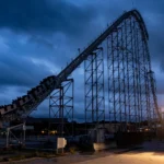 A tall steel roller coaster towering over a theme park at dusk.