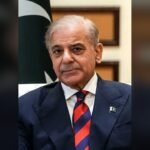 Pakistan's Prime Minister Shehbaz Sharif in a navy suit with a Pakistani flag pin, photographed in front of the Pakistani flag.