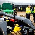 A seized black inflatable dinghy with an outboard motor at the Western Jet Foil site in Dover Harbour, with Border Force officials standing nearby.